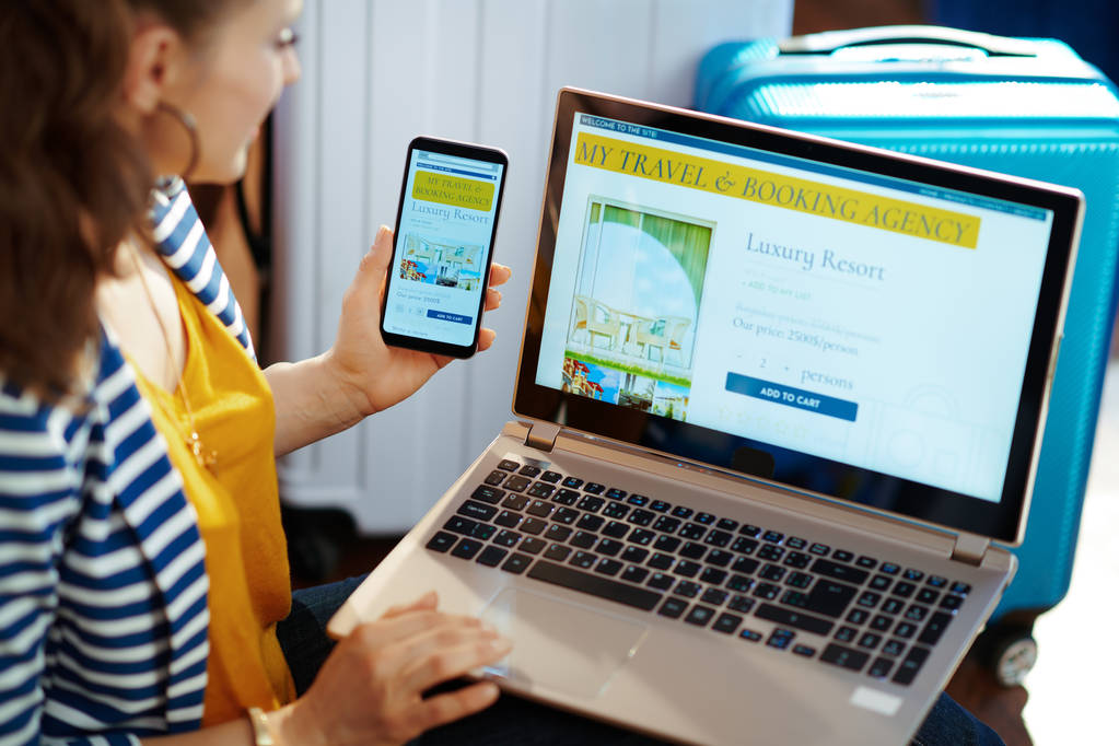 девушка со смартфоном в руке и ноутбуком просматривает страницу сайта и проверяет отклик сайта с оплаченным хостингом